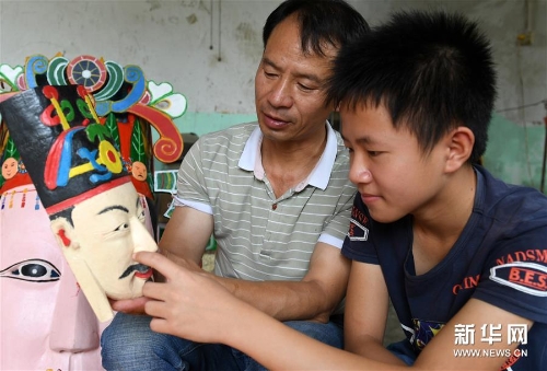 方文展在給兒子方庭源（右）講述毛南族儺面的雕刻技巧