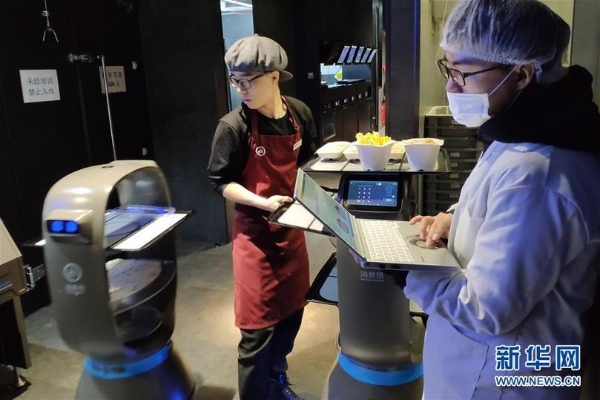 在北京海底撈智慧餐廳，員工（左）在后廚操控送菜機(jī)器人（1月30日手機(jī)拍攝）。