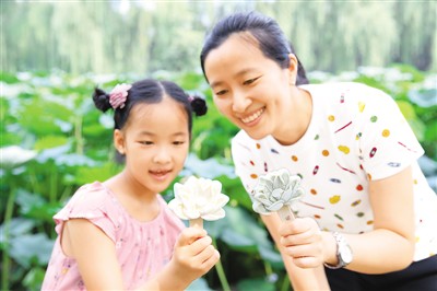 小女孩與家長在北京圓明園遺址公園荷花區(qū)域拿著“荷花冰淇淋”拍照留念。