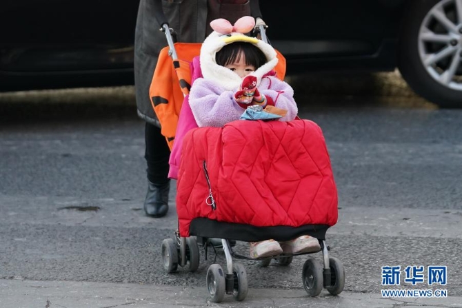 12月29日，在北京朝陽區(qū)青年路和朝陽北路路口，一名小朋友坐在蓋著厚厚衣服的童車上。當(dāng)日，入冬最強(qiáng)寒潮來襲，多地迎來今冬最寒冷天氣。新華社記者鞠煥宗 攝