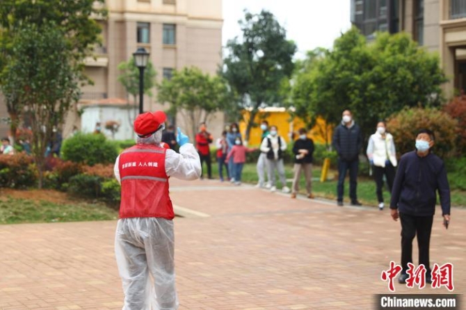 圖為3月19日，穿著紅馬甲的社區(qū)志愿者王娟正拿著小喇叭引導居民有序排隊，維持現(xiàn)場秩序?！⒄祭?攝