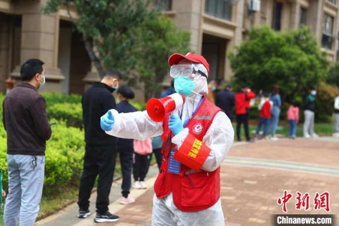 圖為3月19日，穿著紅馬甲的社區(qū)志愿者王娟正拿著小喇叭引導居民有序排隊，維持現(xiàn)場秩序?！⒄祭?攝