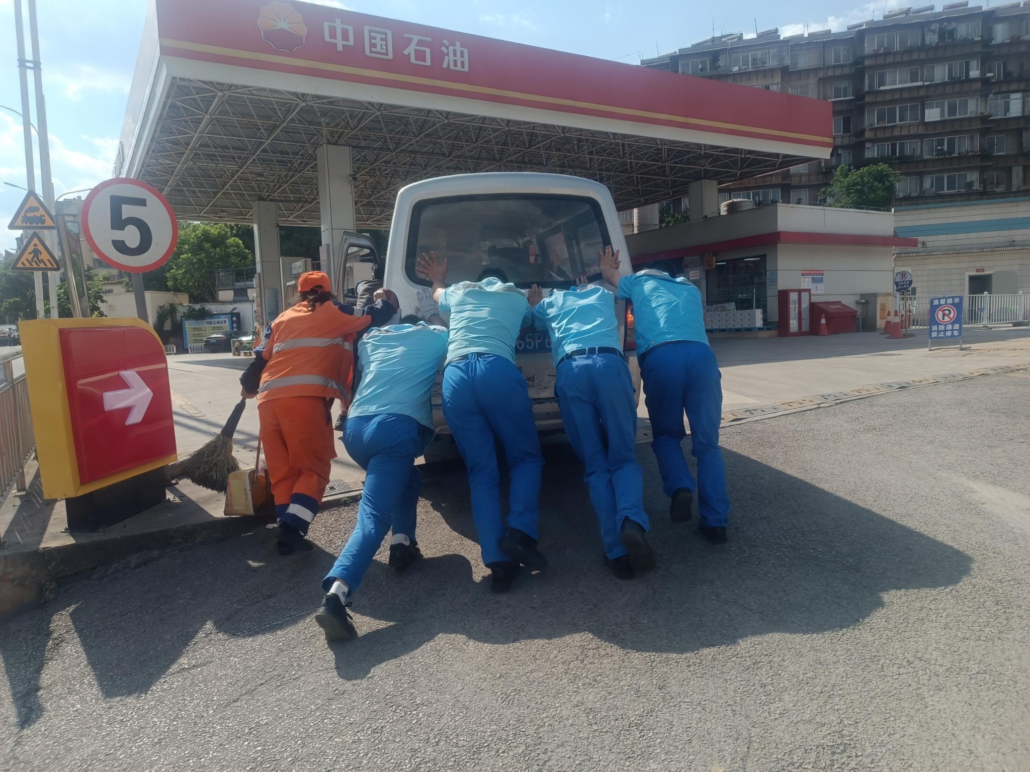 加油站員工和環(huán)衛(wèi)工人幫忙為車輛拋錨顧客推車進站加油