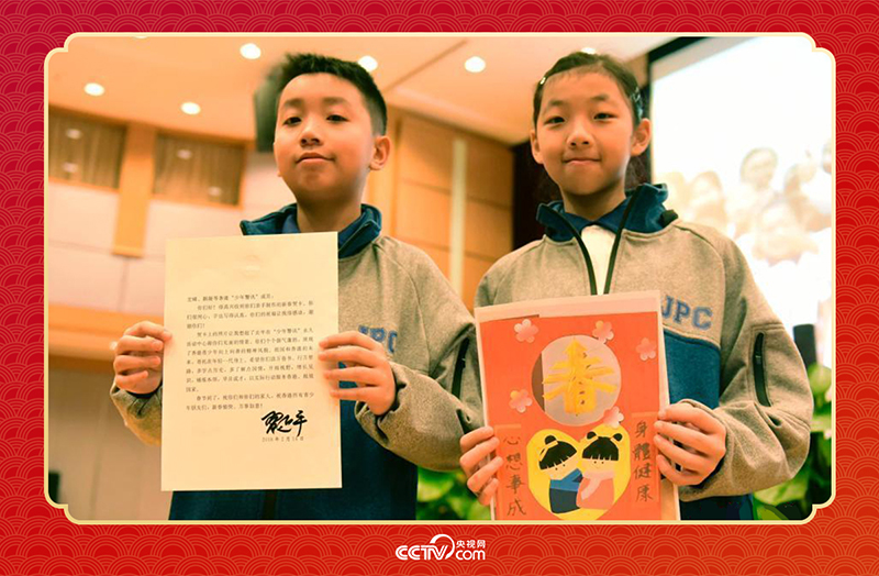 圖為香港“少年警訊”成員郭宏晞（左）展示習(xí)主席回信、羅顥凝（右）展示送給習(xí)主席的賀卡并合影。